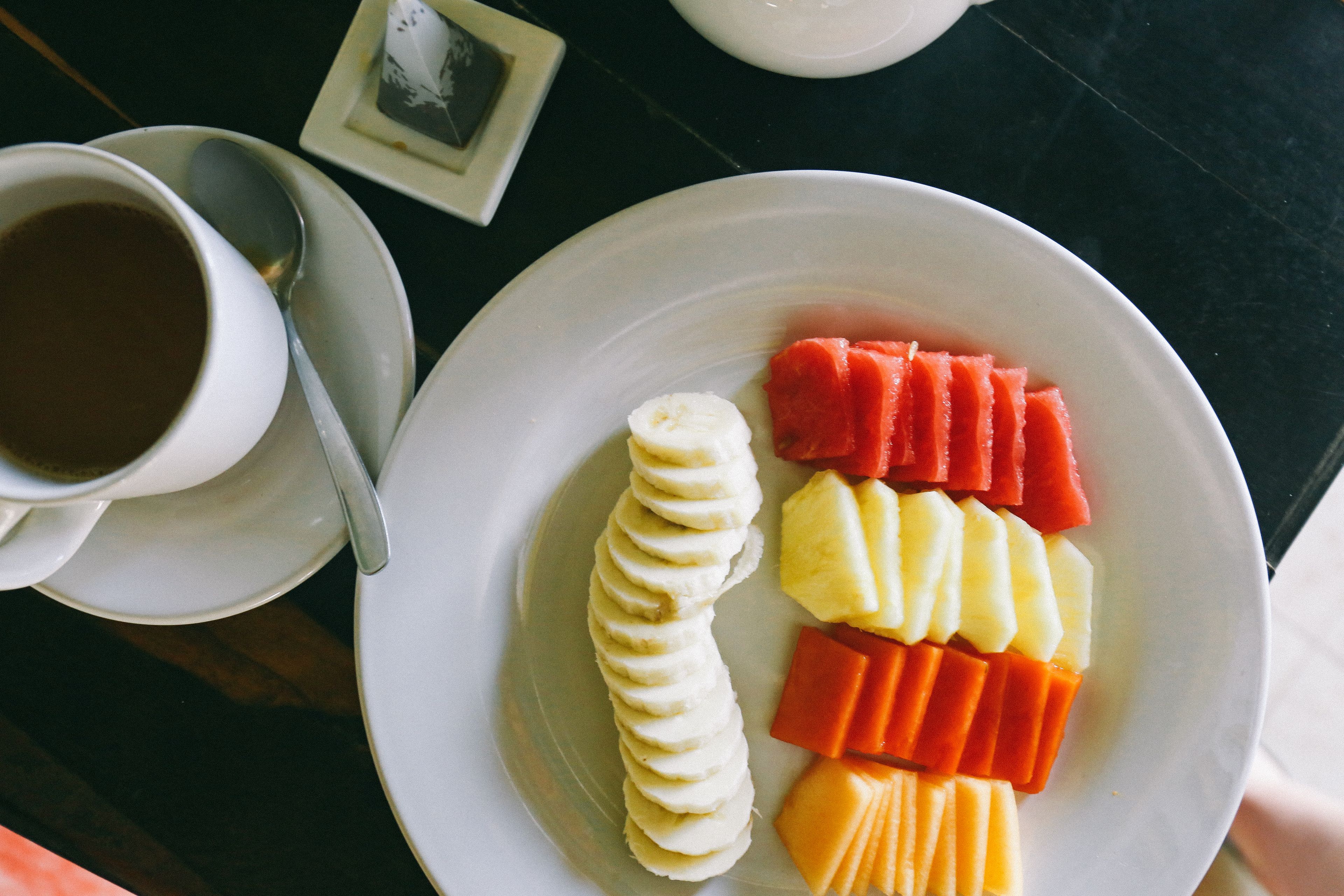 A plate with sliced fruits and a cup of coffee on a table.