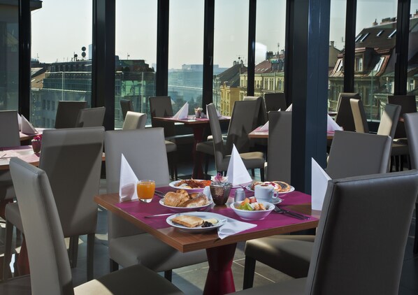 Un comedor con mesas dispuestas para el desayuno, que incluye platos de comida, bebidas y servilletas.