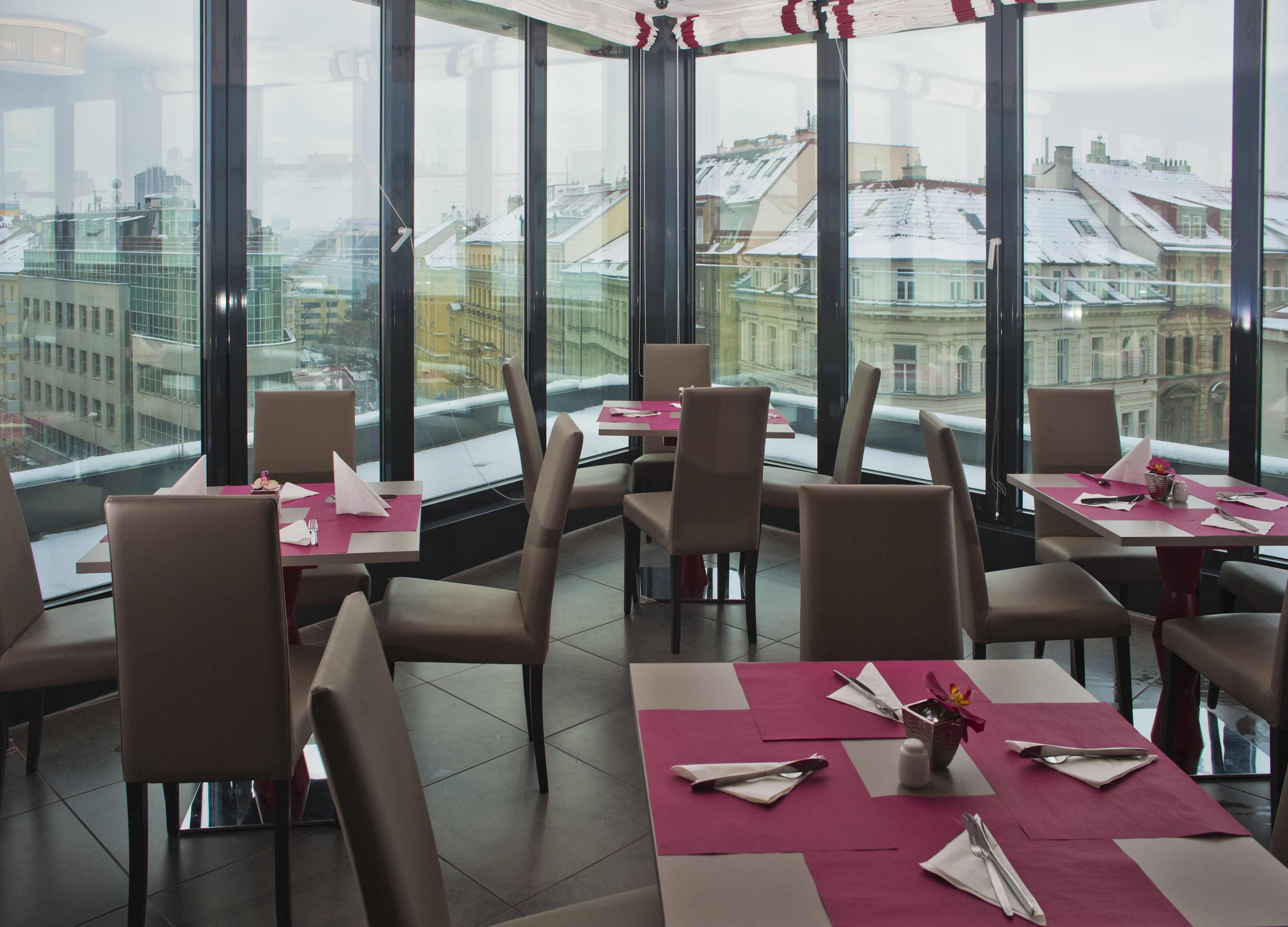 Un restaurante con mesas preparadas para comer, amplias ventanas que ofrecen vistas a edificios y una decoración de interiores moderna.