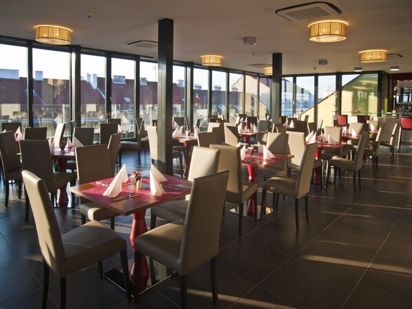 A modern restaurant with large windows, multiple dining tables, and chairs. - Hotel Galileo Prague (Prague)
