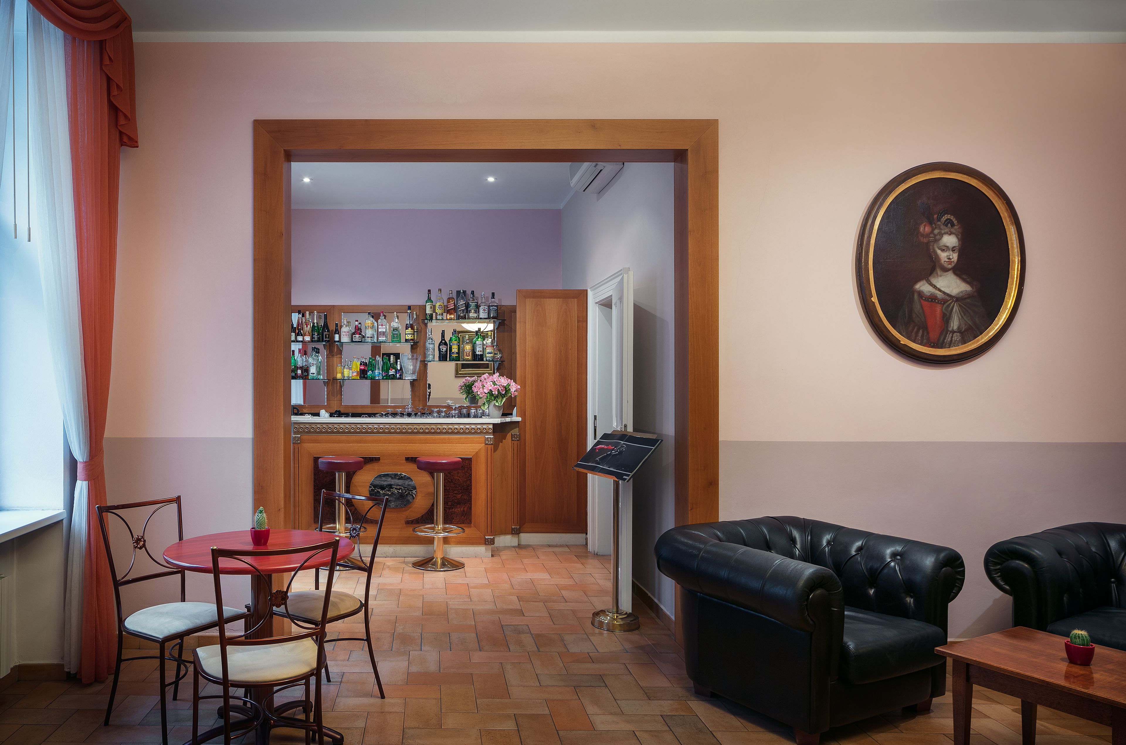 Een bar met verschillende drankflessen, een rode tafel met stoelen en een zwarte leren bank.