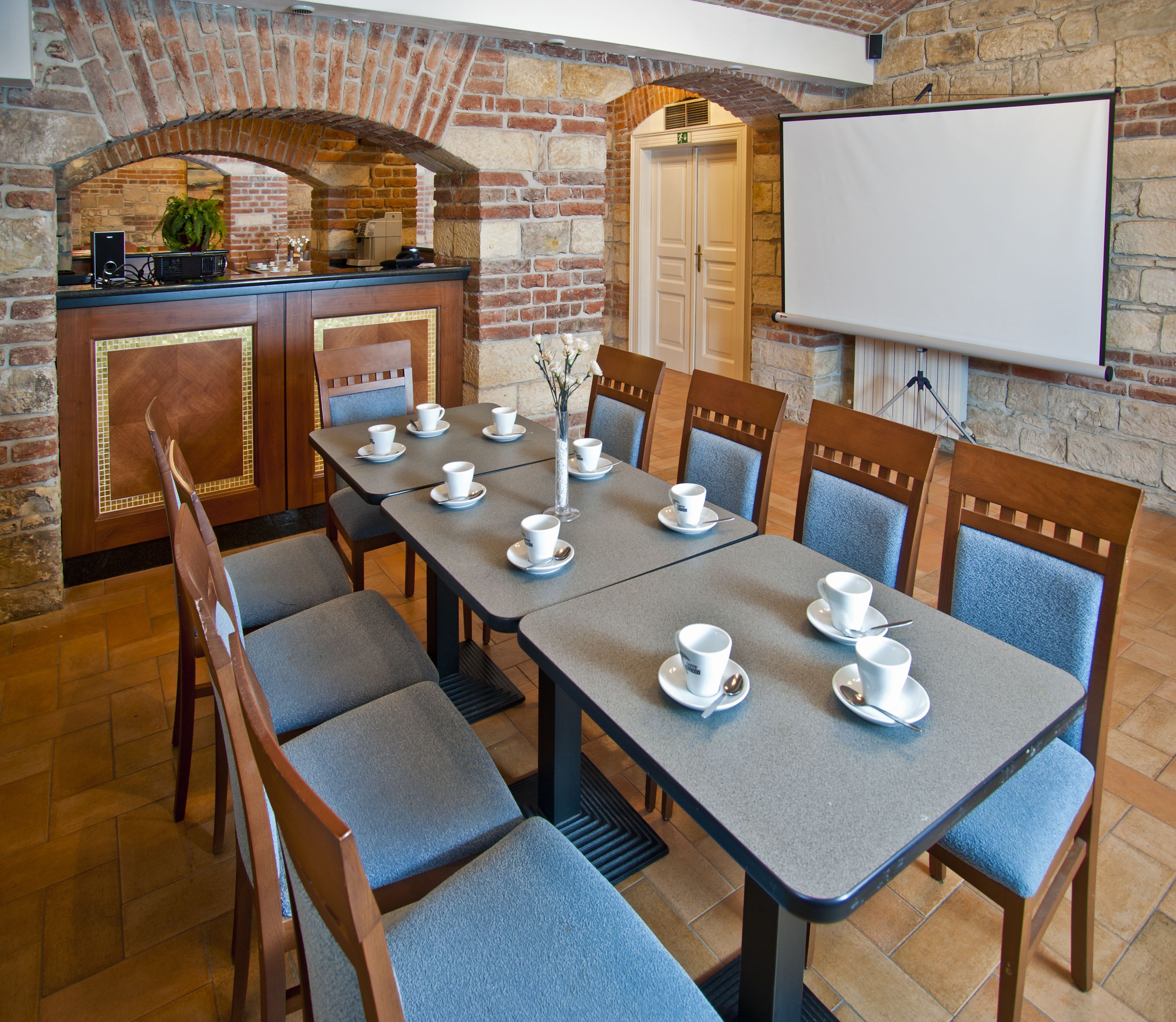 Una sala conferenze con un lungo tavolo, sedie, uno schermo per proiettore e una parete in mattoni.