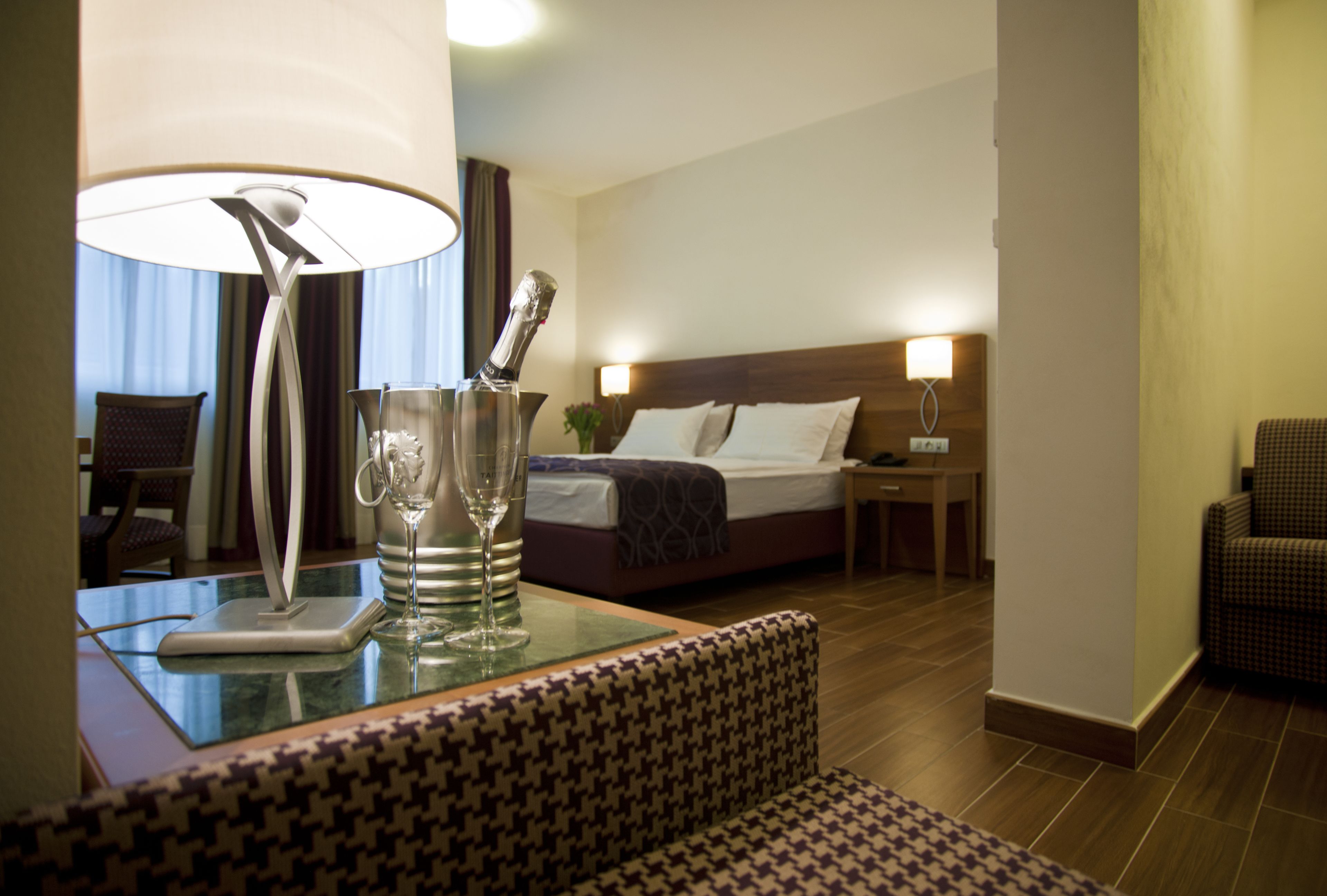 A hotel room with a bed, a nightstand, a lamp, and a seating area with a patterned sofa.