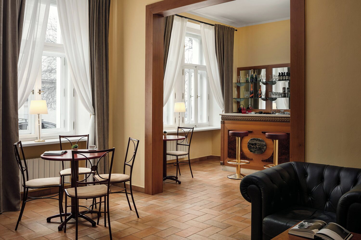 A dining area with two tables and chairs, a bar with a mirror and bottles, and a leather sofa.