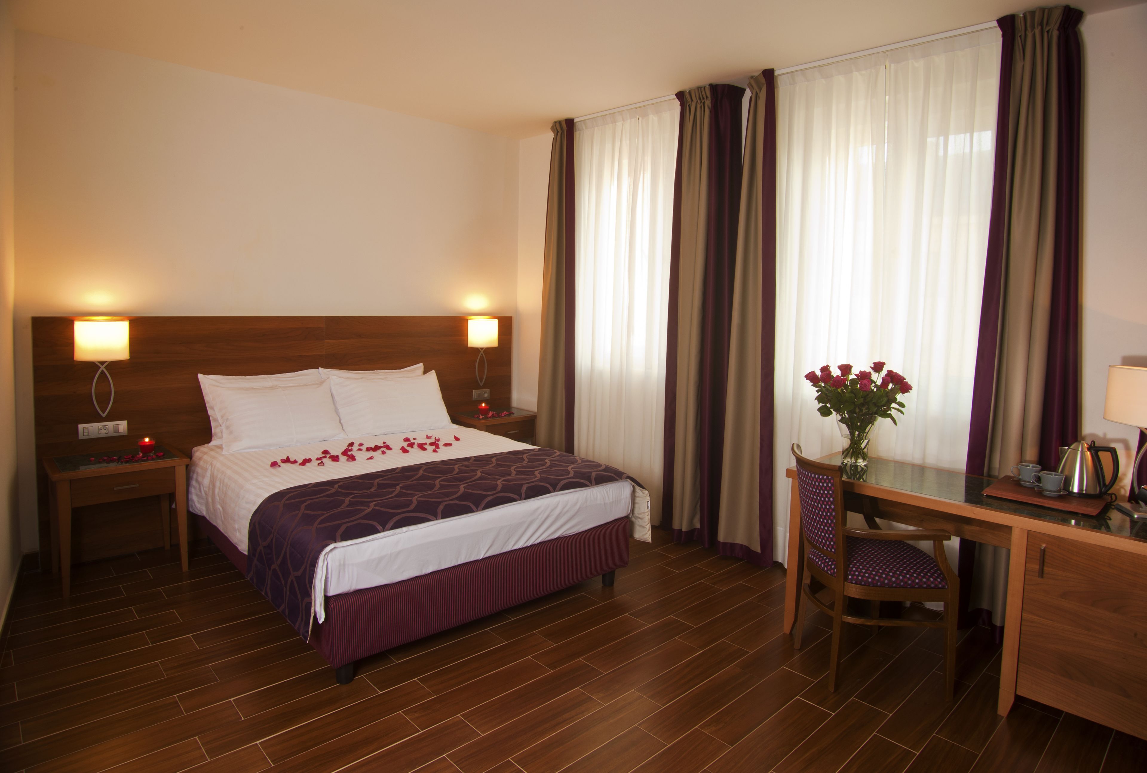 Habitación de hotel con una cama grande, un escritorio y una silla. Hay un florero con flores sobre el escritorio.