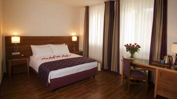 Habitación de hotel con una cama grande, un escritorio y una silla. Hay un florero con flores sobre el escritorio.