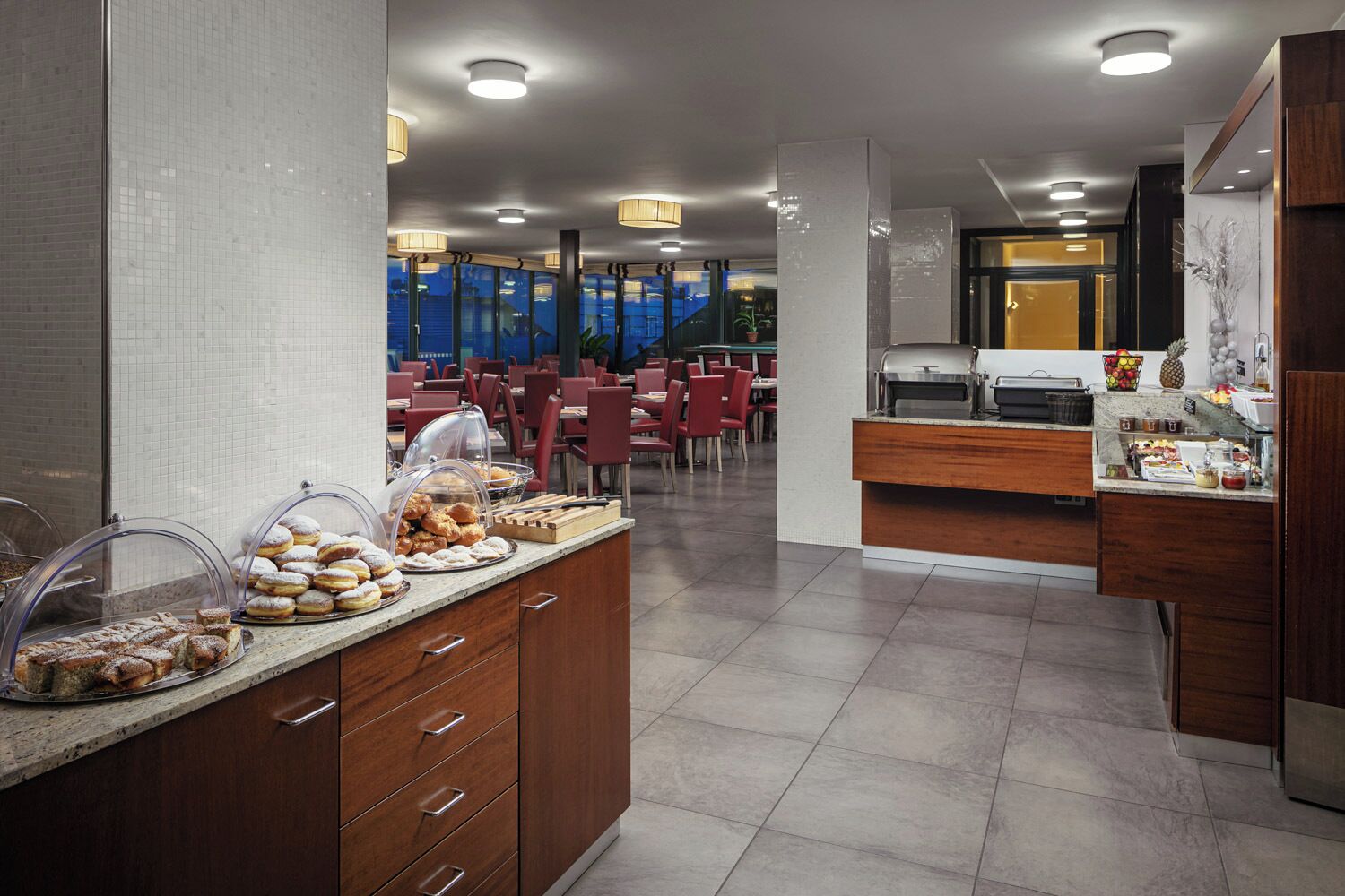 Un comedor moderno de hotel con una barra de buffet, zona de estar y vistas a la ciudad.