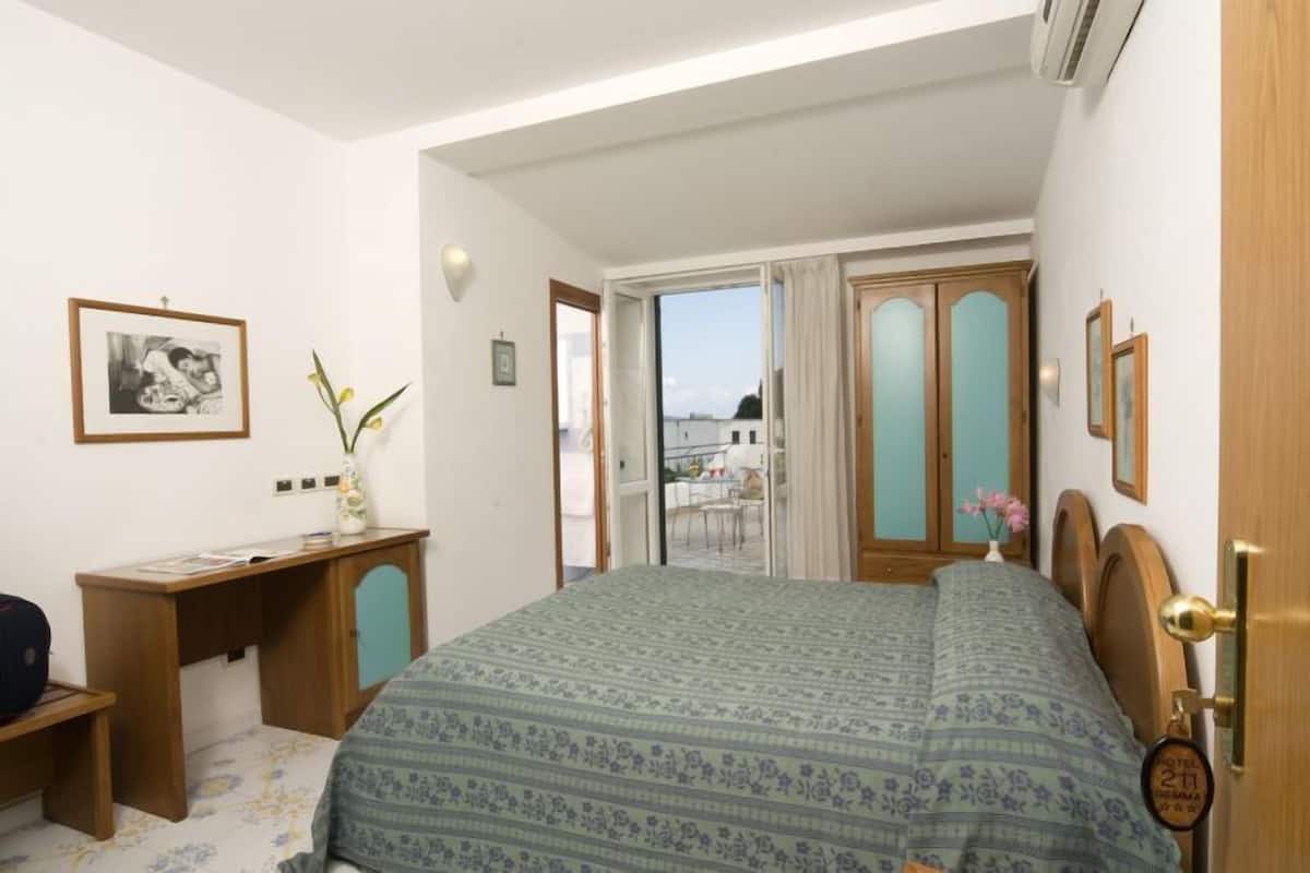 Un dormitorio con cama, escritorio y vista al exterior.