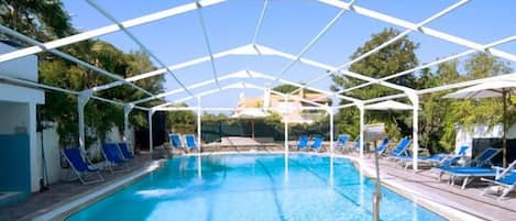 Ein Swimmingpool mit weißer Dachkonstruktion, umgeben von blauen Liegestühlen.