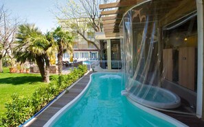 Una piscina con cubierta transparente, rodeada por una terraza de madera y exuberante vegetación.