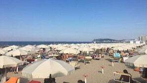 Ein Strand mit zahlreichen weißen Sonnenschirmen und Liegestühlen, typisch für eine Strandhotel-Umgebung.