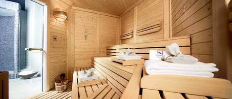 Una sauna de madera con bancos y toallas, una pared de madera y una puerta de vidrio que da a un baño.