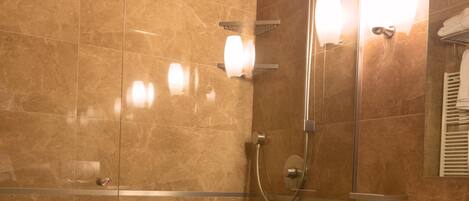 Un baño moderno con ducha de vidrio, lavamanos blanco y espejo con iluminación.