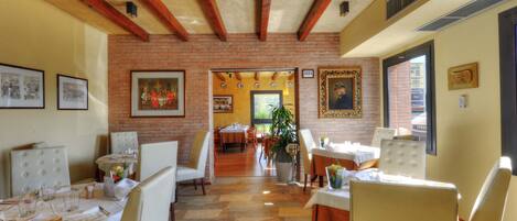 A dining area with brick walls, wooden beams, and tables set for dining.