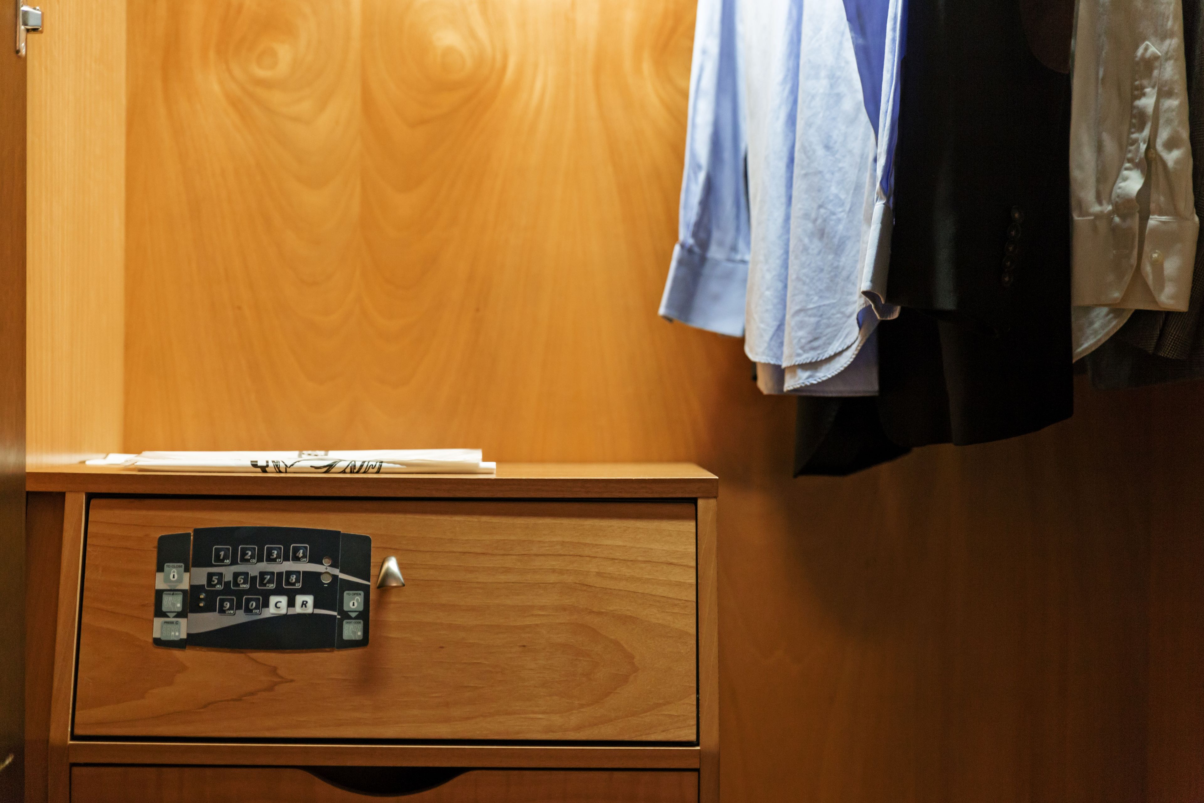 A wooden cabinet with a numeric keypad lock, a hanging garment, and a partially visible curtain.
