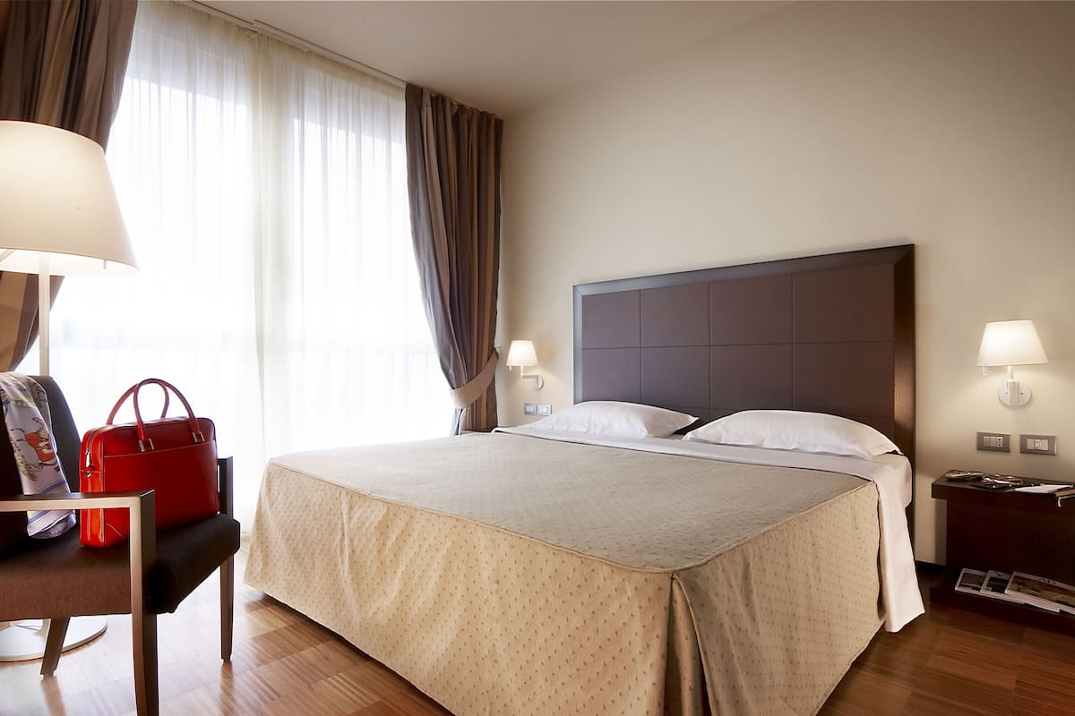 A hotel room with a bed, a chair, a nightstand, and a lamp.