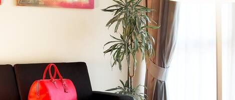 Una sala de estar moderna con un sofá negro, un bolso rojo, una mesa de centro, una lámpara de pie, una planta en maceta y un cuadro en la pared.