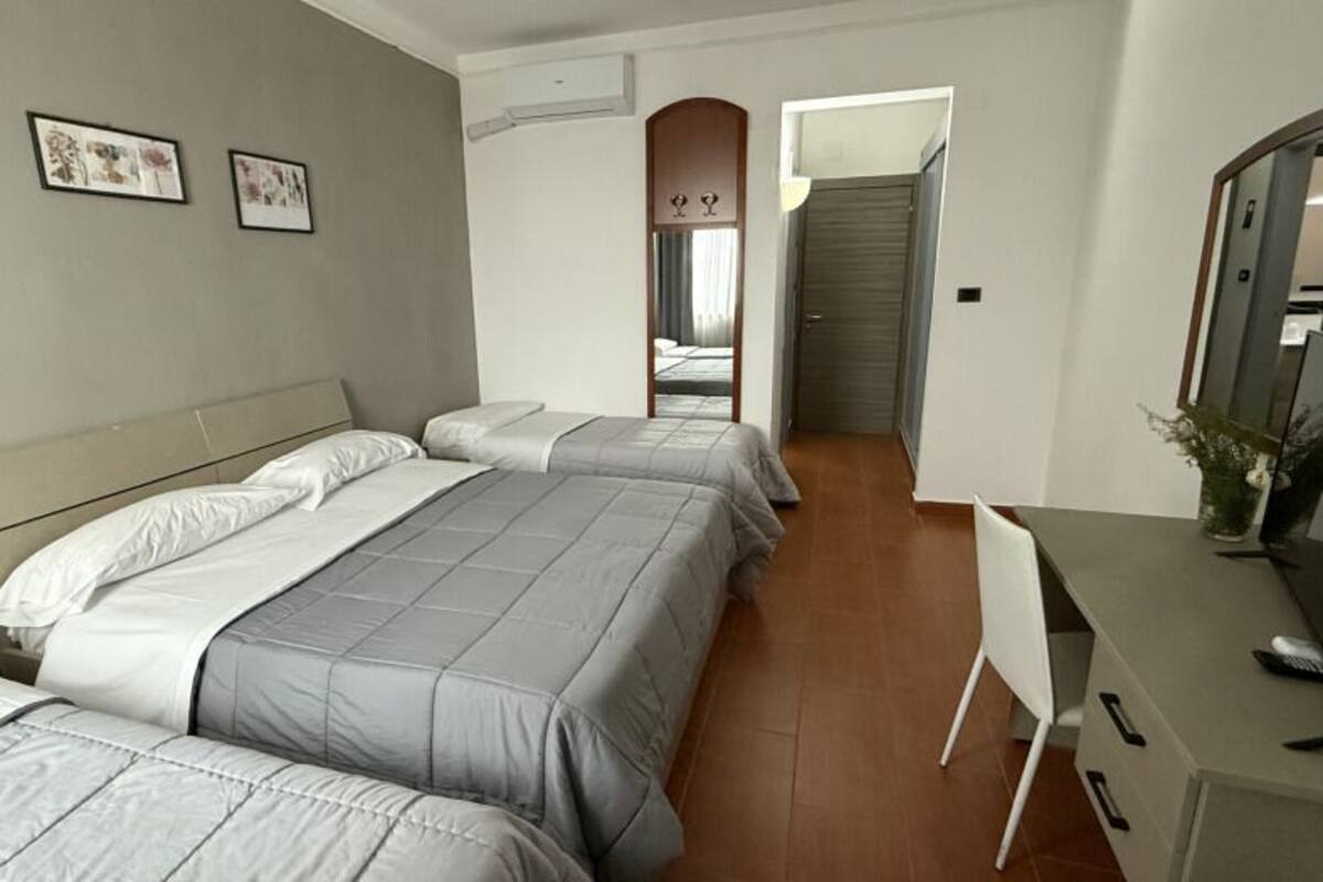 A hotel room with two beds, a desk, and a mirror.