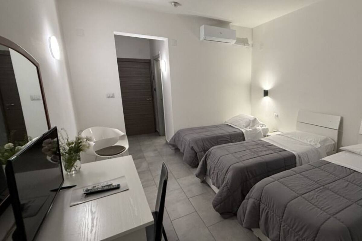 A hotel room with two beds, a desk with a chair, a mirror, and a door.