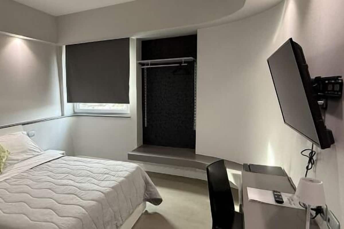 A modern bedroom with a bed, a window, a TV, and a small table.