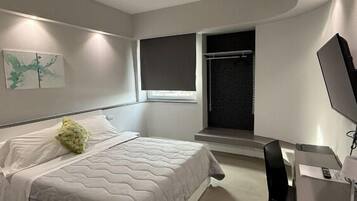 Un dormitorio moderno con una cama, una ventana, un televisor y una mesita.