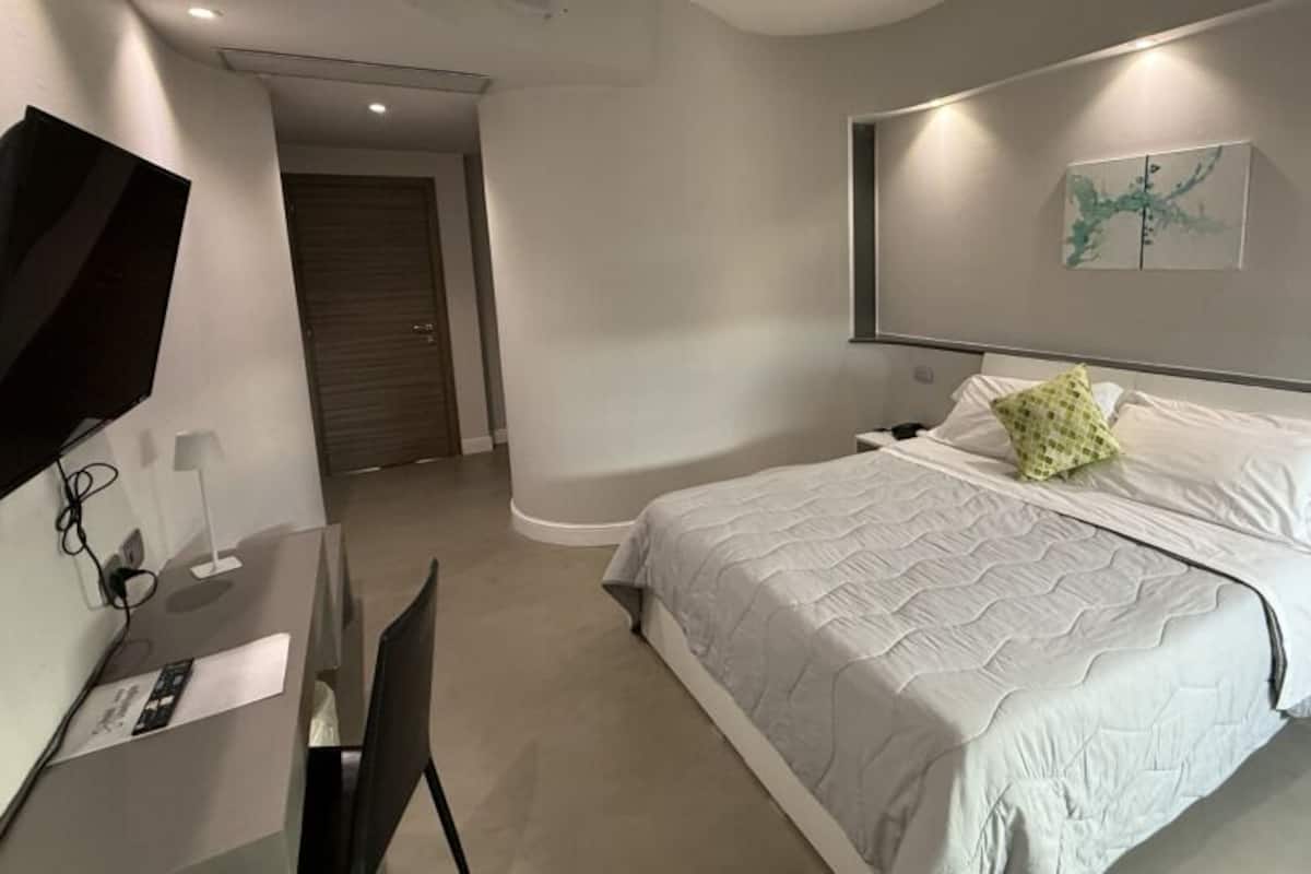A modern bedroom with a bed, bedside tables, a desk, and a TV.