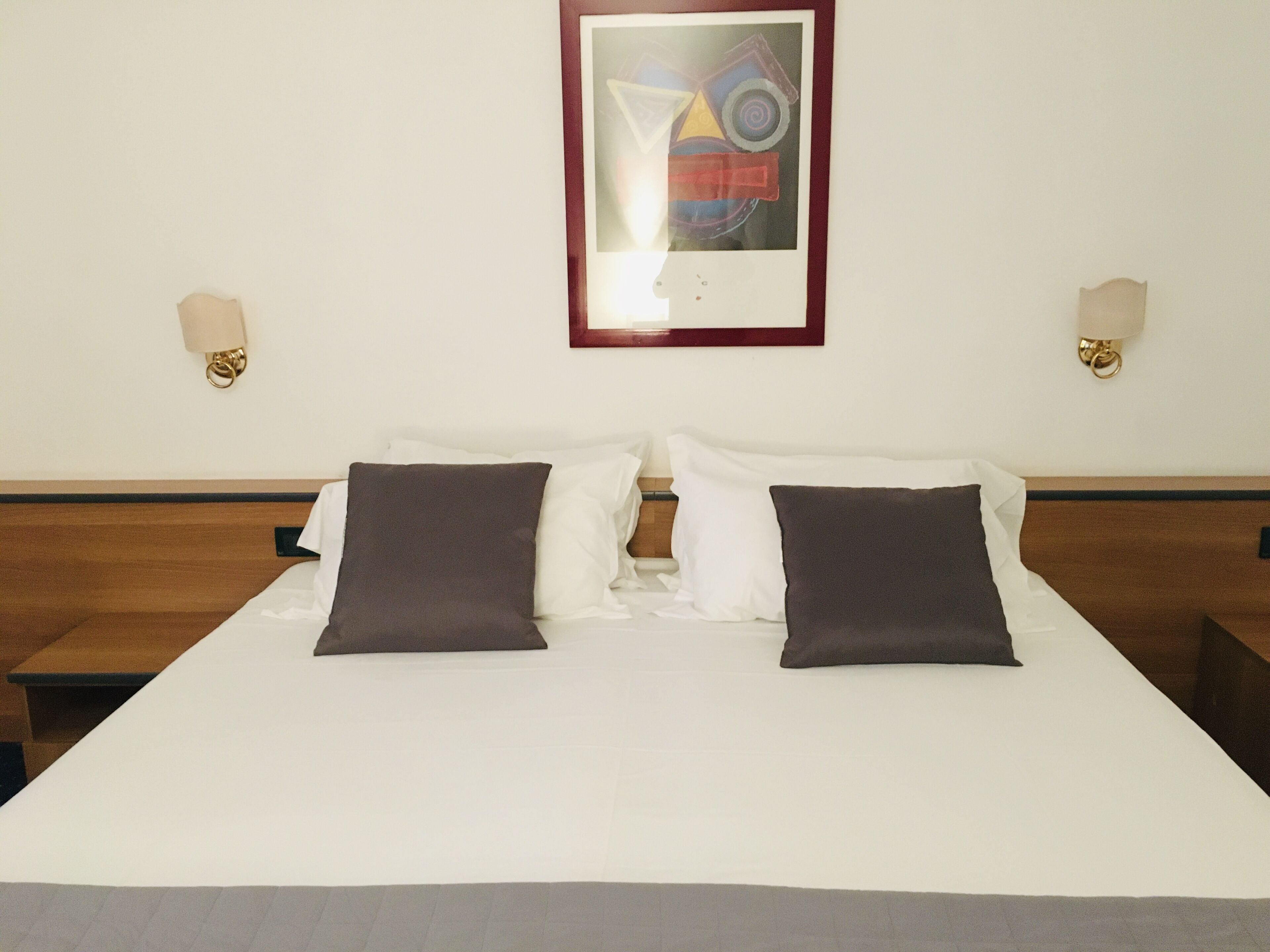 Ein Hotelzimmer mit einem großen Bett, zwei Nachttischen und einem gerahmten abstrakten Gemälde an der Wand.