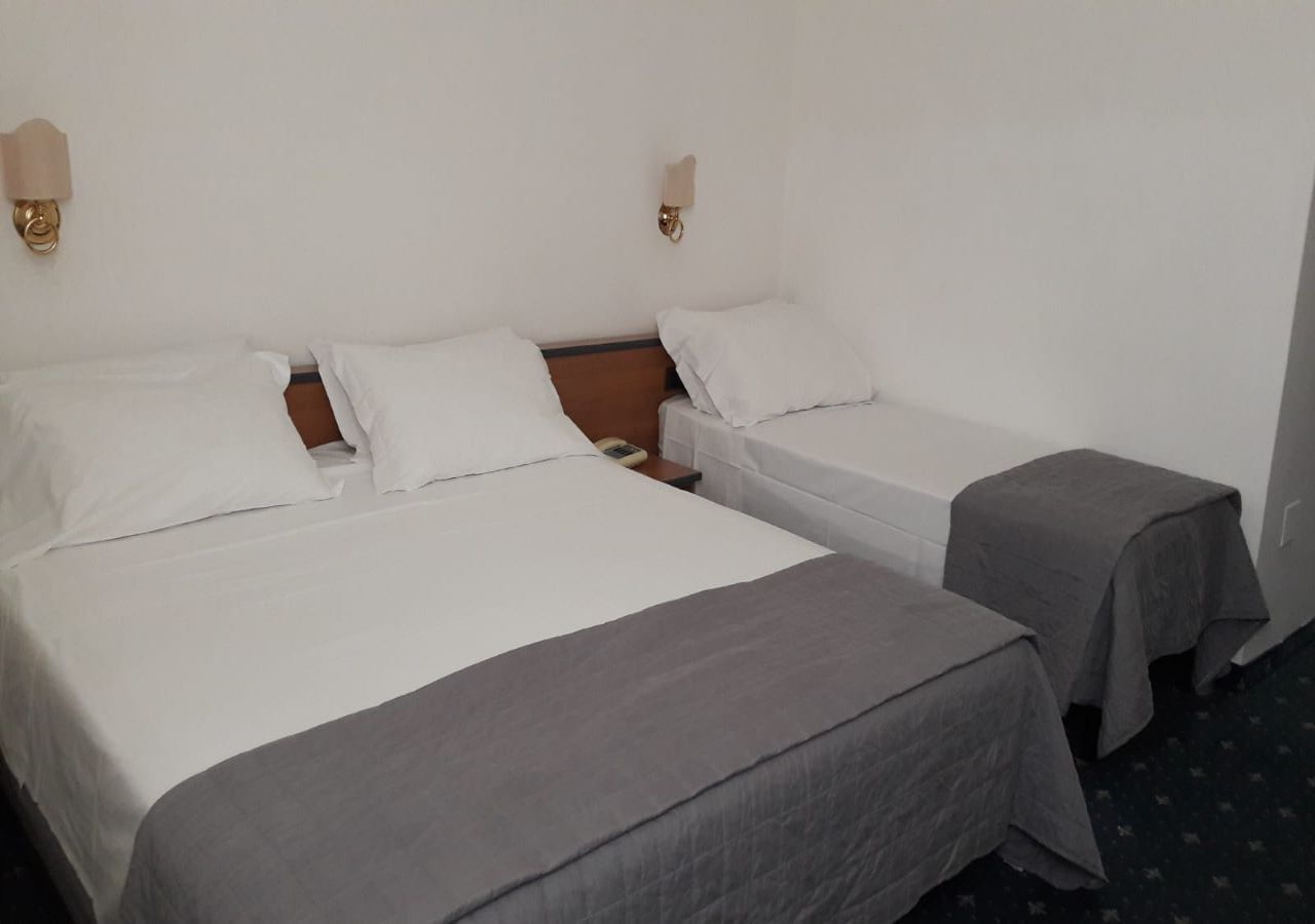 Une chambre d’hôtel avec deux lits, chacun étant équipé de draps blancs et d’une couvre-lit grise. Deux lampes murales sont fixées de chaque côté des lits.