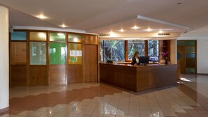 Un área de recepción con un mostrador de madera, una computadora y una ventana con vista a la vegetación.