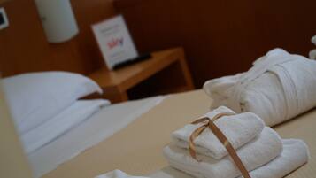 A neatly made bed with white linens and a brown ribbon, a wooden nightstand with a sign, and a wall-mounted light fixture.