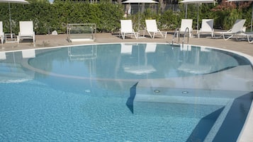 Una piscina cristalina con sillas de descanso blancas y sombrillas alrededor.