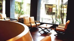 A modern lounge with a curved seating area, large windows offering views of the outdoors, and a small table with a lamp. - HOTEL SELENE POMEZIA (Pomezia)