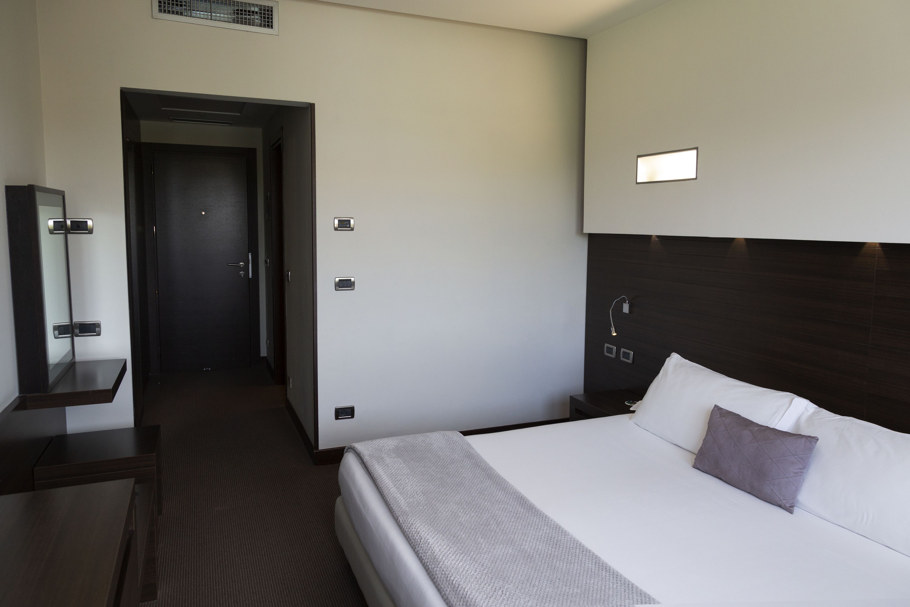 Una habitación de hotel moderna con una cama grande, una mesita de noche, un espejo y una puerta que da a otra habitación.