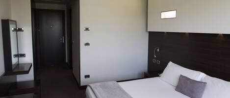 Una habitación de hotel moderna con una cama grande, una mesita de noche, un espejo y una puerta que da a otra habitación.
