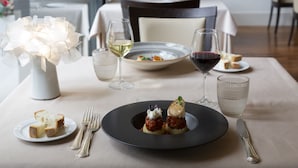 A dining table with a black plate of food, wine glasses, and a vase with white flowers. - HOTEL SELENE POMEZIA (Pomezia)