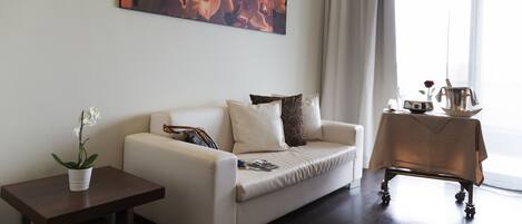 A modern living room with a sofa, a small table with a plant, and a coffee table with a tray.