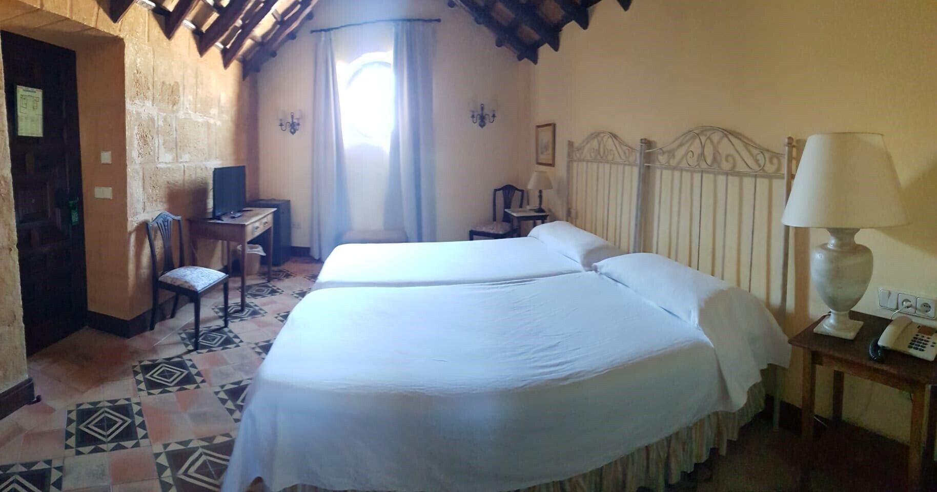 Una habitación de hotel con dos camas, un escritorio, una silla, una lámpara y un teléfono.