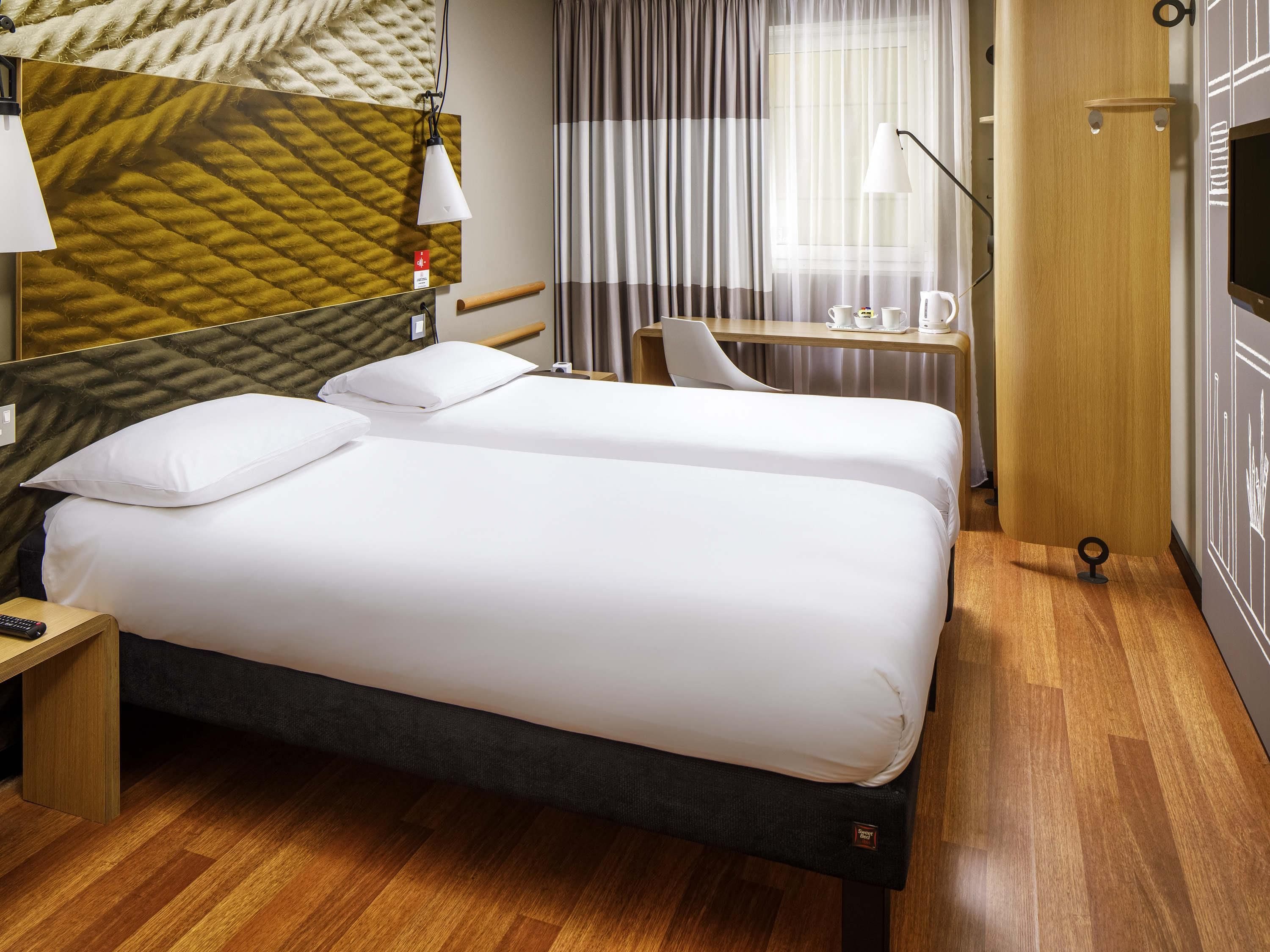 A hotel room with a bed, bedside table, lamp, desk, chair, and a TV.