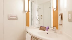 Une salle de bain avec un lavabo blanc, un miroir, une douche et un porte-serviettes.