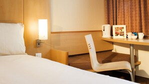 A hotel room with a bed, a desk with a lamp, a chair, and a small table with a card and cups. - ibis Bristol Centre (Bristol)