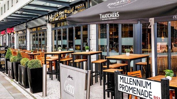 Outdoor seating with tables and chairs, a sign for 'Gem,' and a 'Millenium Promenade' sign. - ibis Bristol Centre (Bristol)
