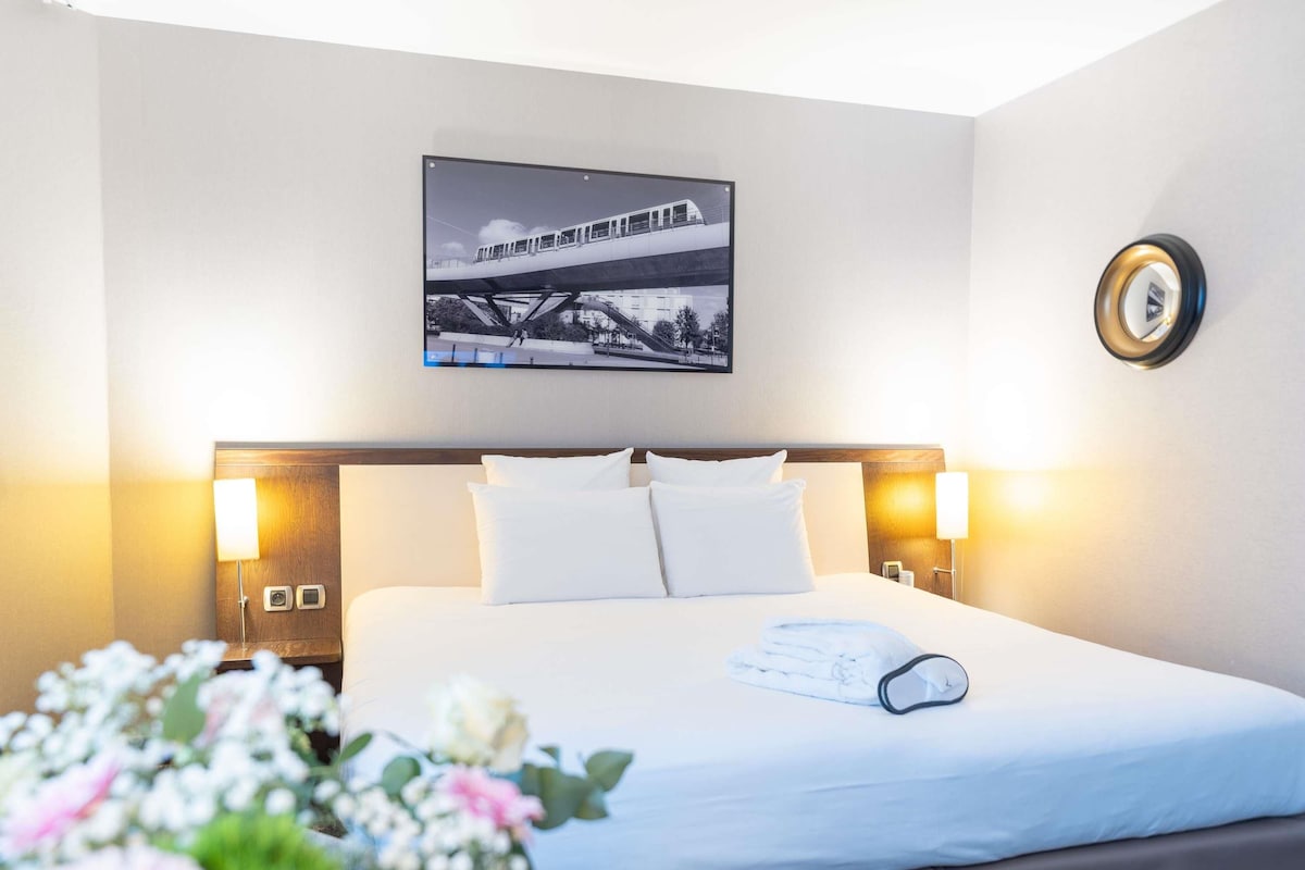 Habitación de hotel con cama, un cuadro en la pared y una mesita de noche con lámpara.