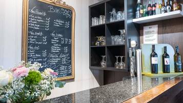 A bar area with a chalkboard menu listing various drinks and their prices, shelves with bottles and glasses, and a counter with a floral arrangement.