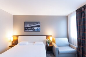A hotel room with a bed, a chair, a nightstand with a lamp, and a framed picture on the wall. - Mercure Rennes Cesson (Cesson-Sevigne)
