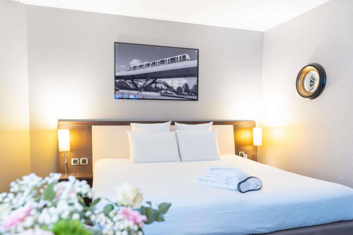 Quarto de hotel com uma cama, um quadro na parede e uma mesa de cabeceira com abajur.
