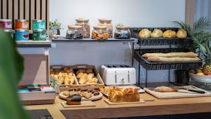 Un bufé con distintos alimentos, entre ellos bollería, pan y frascos con frutos secos y fruta deshidratada.