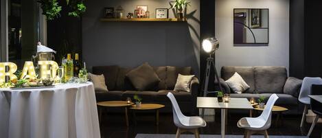 Una sala moderna con un sofá, dos sillas blancas, una mesita y una mesa decorativa con letras iluminadas.