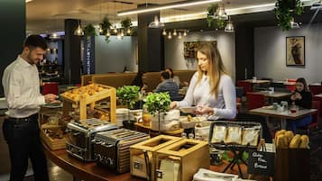 A buffet area with various food items, a sign indicating gluten-free options, and a woman serving food.