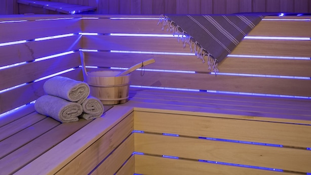 A sauna with wooden benches and benches, a wooden bucket, and a clock on the wall. - Novotel Reading Centre (Reading)