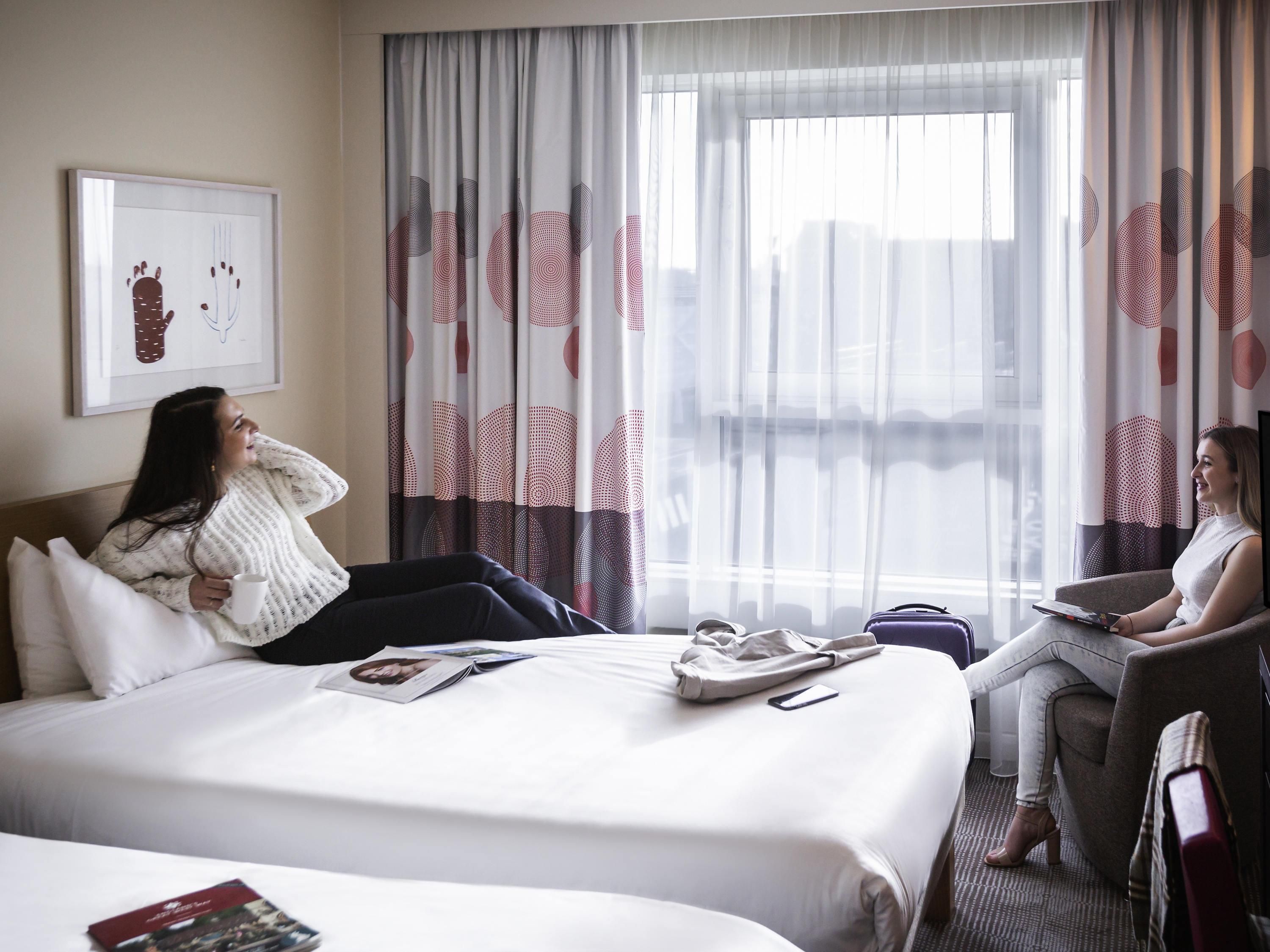 A hotel room with a bed, a sitting area, a window with curtains, and a framed picture on the wall.